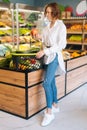 Vertical full length portrait of attractive young customer woman holding pomegranate standing with basket of fruits and Royalty Free Stock Photo