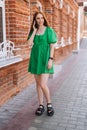 Vertical full length portrait of cheerful young woman talking on mobile phone standing on city street in summer day