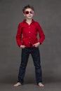 Vertical full-length portrait of a stylish little boy in red sunglasses