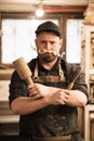 Vertical funny businessman, carpenter in cap, apron with shaving chip mustache under nose, holding chisel, mallet tools