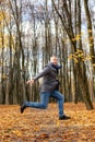 Vertical funny excited powerful mature grizzled businessman jump on one leg with raised leg and arms, levitating in park