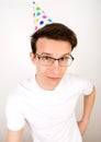 A vertical funny photo of a young guy in a festive hat, white shirt and glasses with a thoughtful look right into the camera