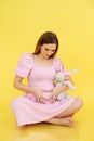 Vertical glad tranquil calm pregnant barefoot woman sitting floor in pink dress with hair rabbit toy. Its girl waiting