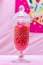 A vertical glass Jar full of red colour / color small candies on pink background