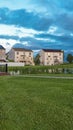 Vertical Grassy park with pond bridge trees and bench in front of multi storey homes