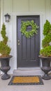 Vertical Gray front door of a home with green wreath and flanked by tall potted plants Royalty Free Stock Photo