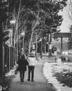 Vertical grayscale of a couple walking on the sidewalk partially covered with snow