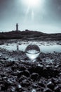 Vertical grayscale shot of a crystal ball with a lighthouse on the rocky seashore