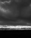 Vertical grayscale shot of dark thunder sky over silhouettes of wind turbines