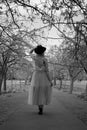 Vertical grayscale shot of a woman walking in a pathway in a garden with trees Royalty Free Stock Photo