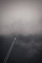 Vertical greyscale shot of an airplane leaving a trail in the sky