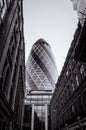 Vertical greyscale of the 30 St Mary Axe surrounded by buildings under the sunlight in London