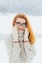 Vertical half-length portrait of the charming smiling red head woman wearing glasses is wrapped in the knitted scarf in Royalty Free Stock Photo