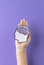 Vertical of hands holding head silhouette with purple brain on purple background, with copy space