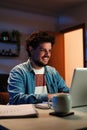 Vertical. Happy freelancer man working at home with laptop on a desk at night. Young guy smiling and browsing on Royalty Free Stock Photo