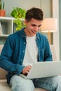 Vertical. Happy freelancer man working at home with a laptop on a sofa. Young guy smiling and browsing on internet using Royalty Free Stock Photo