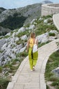 Vertical high-angle of rear of female tourist walking on the path leading to rocky mountains