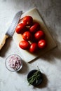 Vertical high angle shot of tomatoes on a white chopping board near a knife and chopped onions Royalty Free Stock Photo