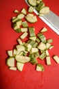 Vertical high angle view of zucchini cubes on a red board with a knife on it under the lights