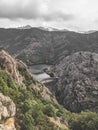 Vertical high shot of high rocks covered in greenery and a view of a lake under a cloudy sky