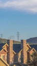 Vertical Homes with gray gable roofs and stone brick chimneys against mountain and sky