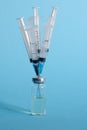 A vertical image of an ampoule with a drug and five medical syringes stuck in the bottle cap on a blue isolated background. The