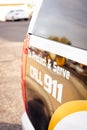 Vertical image of back end of a police car vehicle reading Protect and serve call 911