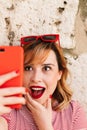 Vertical image of a beautiful woman smiling and taking a selfie in the street with her smartphone for her social networks.