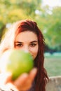 Vertical image of a beautiful young red-haired woman, holding a green apple outdoors and looking at the camera Royalty Free Stock Photo