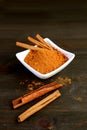 Vertical image of bowl of ground cinnamon powder with cinnamon stick on black wooden background Royalty Free Stock Photo