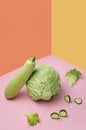 Vertical image.Chopped cucumber, cabbage, fresh marrow and salad leaves on the pink surface against yellow and orange background