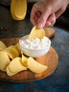 Vertical image close-up of a man dips potato chips into sauce in a white bowl on a wooden cutting board Royalty Free Stock Photo