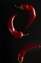 Vertical image.Closeup of flying red chili pepper against blackbackground