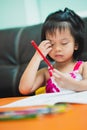 Vertical image. Cute girl is scratching her face due to itching as she sits painting on the table