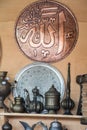 Vertical image of decorative brass jars and plates with the word Allah in Arabic calligraphy