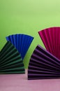 Vertical image.Different colors of papaer fan on the pink surface against green background.Empty space