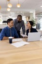 Vertical image of diverse female and male businesspeople working on laptop in office