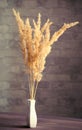 Vertical image of dry field spikelets young reed grass in a white vase on the wooden surface of the table