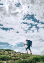 Vertical image of female backpacker climbing to the mountain top using trekking poles with bright cloudscape background. Active Royalty Free Stock Photo