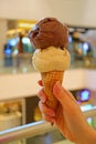 Vertical image of hand holding ice cream cone with two scoops of chocolate and peanut butter ice