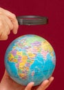 Vertical image of a hand holding a magnifying glass over an world globe Royalty Free Stock Photo