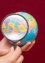 Vertical image of a hand holding a magnifying glass over an world globe Royalty Free Stock Photo