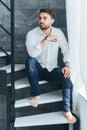 Vertical image of handsome bearded man sitting on stairs in loft. Holding smartphone in hands. Thinking about new ideas Royalty Free Stock Photo