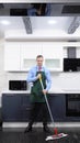 Vertical image. handsome man in tie and apron mops the floor in the kitchen