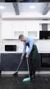 A vertical image. handsome man in tie and apron sweeping the kitchen floor Royalty Free Stock Photo