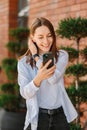 Vertical image of happy smiling young woman typing on smartphone over city background Royalty Free Stock Photo