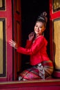 Vertical image of lovely Asian Thai woman wear Thai Lanna traditional style sit at the red door of ancient building and look at Royalty Free Stock Photo