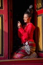 Vertical image of lovely Asian Thai woman wear Thai Lanna traditional style sit at the red door of ancient building and look at Royalty Free Stock Photo