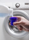 Vertical image.Man holding a cup and pouring liquid laundry detergent against washing machine.Household routine