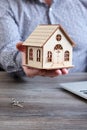 Vertical image a man holds a small wooden house in his hand against the background of a table with keys and a laptop Royalty Free Stock Photo